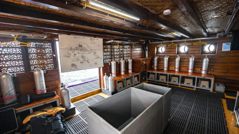 Dive deck of a wooden liveaboard with cylinders racked and gear stowed along the bulwark