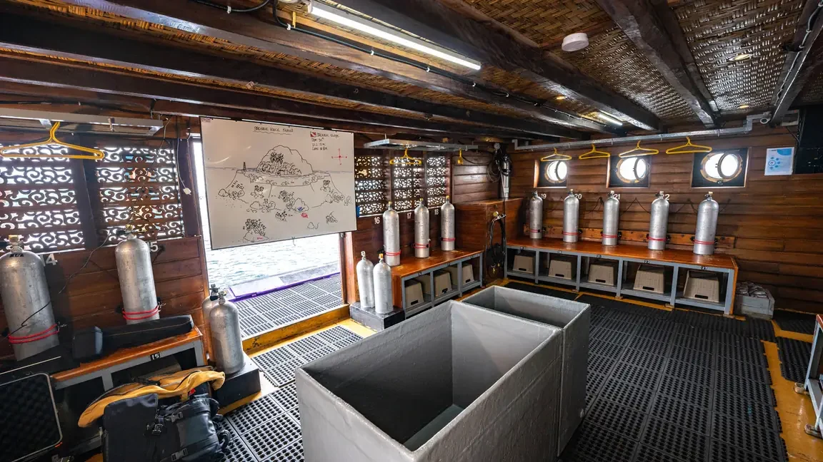 Dive deck of a wooden liveaboard with cylinders racked and gear stowed along the bulwark