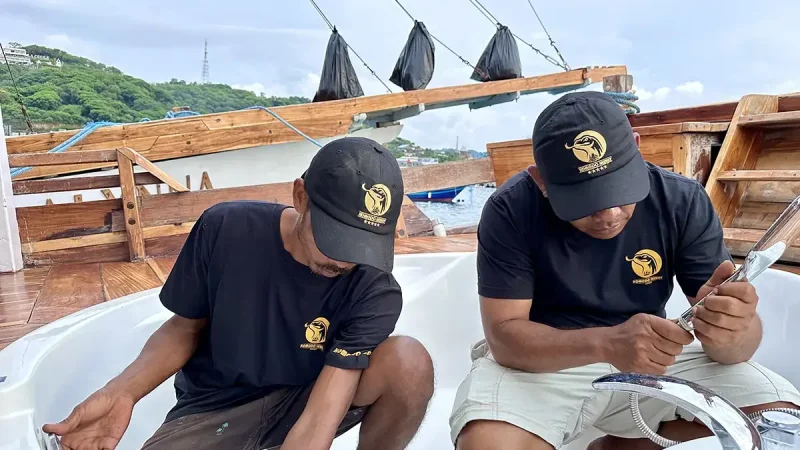 Dua tukang bekerja berdampingan menyelesaikan pemasangan perlengkapan di atas kapal kayu