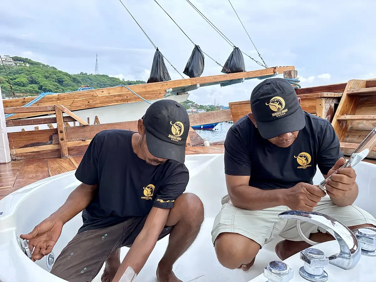 Dua tukang bekerja berdampingan menyelesaikan pemasangan perlengkapan di atas kapal kayu
