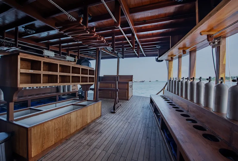 Dive deck of a wooden liveaboard with cylinders racked along the timber bulwark