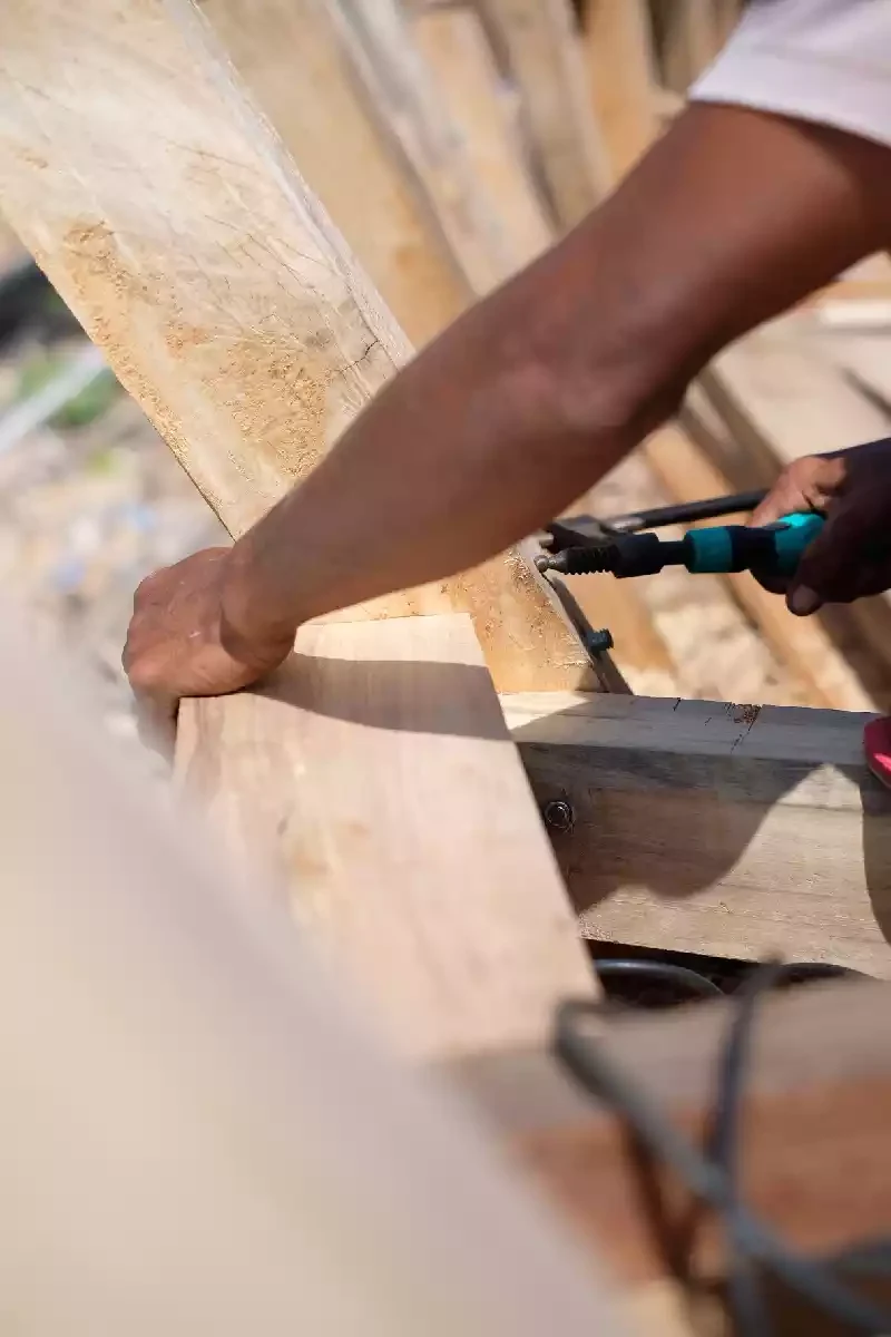Shipwright's hands working a tool along the planking of a wooden hull