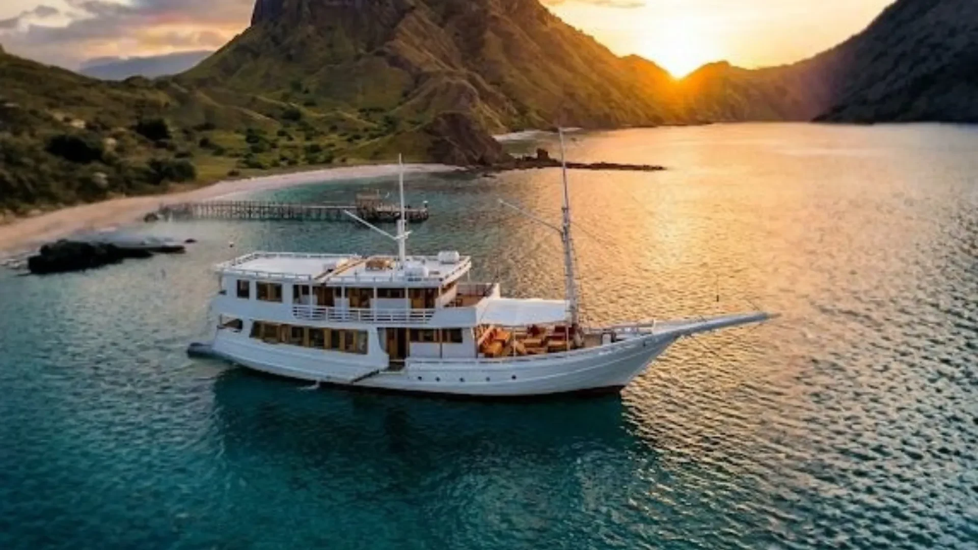 Wooden liveaboard phinisi lying at anchor off a Komodo headland in low evening light