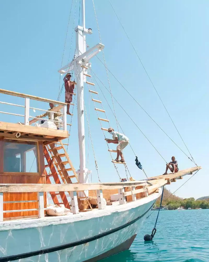 Crew working aloft on the mast and bowsprit of a wooden liveaboard phinisi lying at anchor
