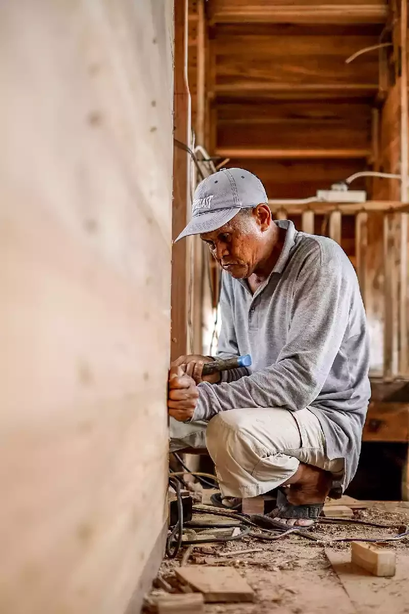 Shipwright crouched inside the shell of a hull, fitting a frame against the planking