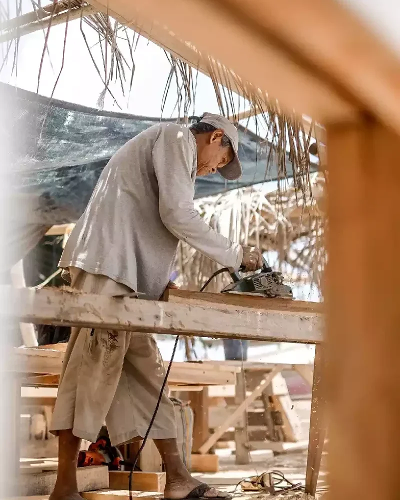 Shipwright working underneath a wooden hull supported on timber props